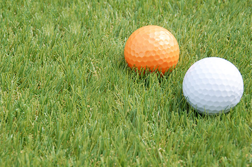 人工芝の上にオレンジと白のゴルフボール